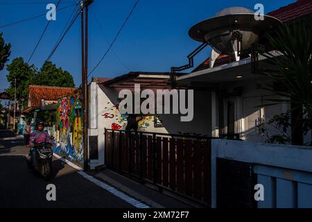 26 juillet 2024, Yogyakarta, région spéciale de Yogyakarta, Indonésie : un motocycliste passe devant une murale sur le thème des OVNIS et des extraterrestres dans le village des OVNIS dans le district de Mantrijeron, ville de Yogyakarta. Les résidents ont collaboré pour décorer le village avec un thème OVNI et extraterrestre pour accueillir le jour de l'indépendance de la République d'Indonésie le 17 août. En outre, le village OVNI est conçu comme un langage pour étudier l'univers, de sorte que les gens sont toujours conscients de maintenir la propreté dans leurs environnements respectifs. (Crédit image : © Angga Budhiyanto/ZUMA Press Wire/Alamy Live News) USAGE ÉDITORIAL SEULEMENT! Banque D'Images
