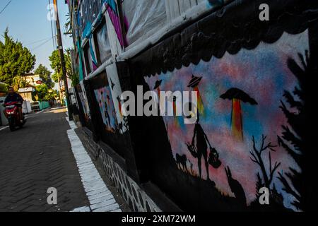 26 juillet 2024, Yogyakarta, région spéciale de Yogyakarta, Indonésie : un motocycliste passe devant une murale sur le thème des OVNIS et des extraterrestres dans le village des OVNIS dans le district de Mantrijeron, ville de Yogyakarta. Les résidents ont collaboré pour décorer le village avec un thème OVNI et extraterrestre pour accueillir le jour de l'indépendance de la République d'Indonésie le 17 août. En outre, le village OVNI est conçu comme un langage pour étudier l'univers, de sorte que les gens sont toujours conscients de maintenir la propreté dans leurs environnements respectifs. (Crédit image : © Angga Budhiyanto/ZUMA Press Wire/Alamy Live News) USAGE ÉDITORIAL SEULEMENT! Banque D'Images