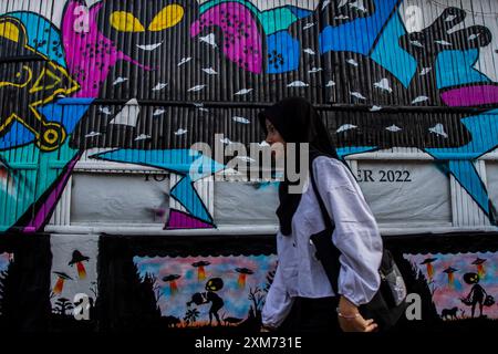 26 juillet 2024, Yogyakarta, région spéciale de Yogyakarta, Indonésie : une femme marche près d'une murale avec un OVNI et une murale sur le thème des extraterrestres dans le village des OVNIS dans le district de Mantrijeron, ville de Yogyakarta. Les résidents ont collaboré pour décorer le village avec un thème OVNI et extraterrestre pour accueillir le jour de l'indépendance de la République d'Indonésie le 17 août. En outre, le village OVNI est conçu comme un langage pour étudier l'univers, de sorte que les gens sont toujours conscients de maintenir la propreté dans leurs environnements respectifs. (Crédit image : © Angga Budhiyanto/ZUMA Press Wire/Alamy Live News) USAGE ÉDITORIAL Banque D'Images