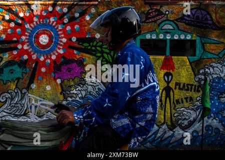 26 juillet 2024, Yogyakarta, région spéciale de Yogyakarta, Indonésie : un conducteur de pousse-pousse passe devant une murale avec un OVNI et une murale sur le thème des extraterrestres dans le village des OVNIS dans le district de Mantrijeron, ville de Yogyakarta. Les résidents ont collaboré pour décorer le village avec un thème OVNI et extraterrestre pour accueillir le jour de l'indépendance de la République d'Indonésie le 17 août. En outre, le village OVNI est conçu comme un langage pour étudier l'univers, de sorte que les gens sont toujours conscients de maintenir la propreté dans leurs environnements respectifs. (Crédit image : © Angga Budhiyanto/ZUMA Press Wire/Alamy Live News) ÉDITEUR Banque D'Images