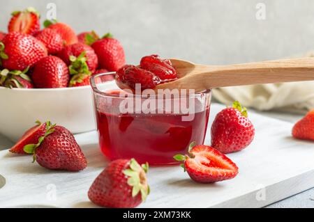 Verre de confiture de fraises dans une cuillère en bois sur une table rustique blanche Banque D'Images