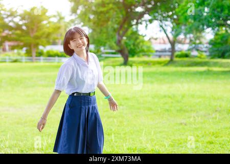 Portrait mignon charmant heureux heureux étudiant asiatique uniforme fille debout dans le parc vert en plein air souriant Banque D'Images