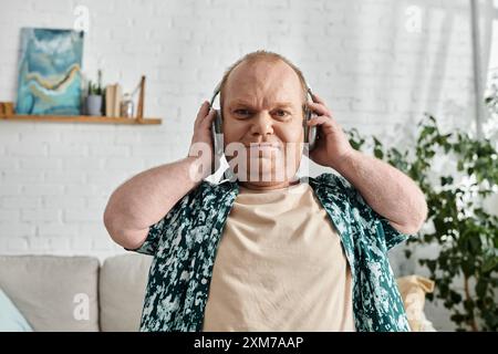 Un homme avec inclusivité portant des écouteurs écoute de la musique à l'intérieur. Banque D'Images