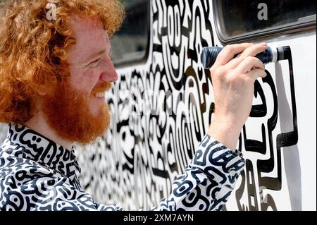 Tenterden, Kent, Royaume-Uni. 26 juillet 2024. L'artiste de renommée internationale Mr Doodle (Sam Cox) crée le premier train Doodle au monde, couvrant un wagon de 64 pieds avec ses griffes signature - pour marquer le 50e anniversaire du chemin de fer Kent et East Sussex, à sa base à la gare de Tenterden dans sa ville natale. Crédit : Phil Robinson/Alamy Live News Banque D'Images