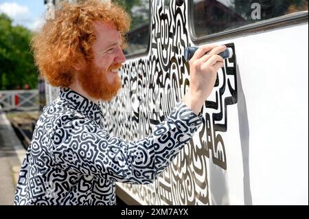 Tenterden, Kent, Royaume-Uni. 26 juillet 2024. L'artiste de renommée internationale Mr Doodle (Sam Cox) crée le premier train Doodle au monde, couvrant un wagon de 64 pieds avec ses griffes signature - pour marquer le 50e anniversaire du chemin de fer Kent et East Sussex, à sa base à la gare de Tenterden dans sa ville natale. Crédit : Phil Robinson/Alamy Live News Banque D'Images