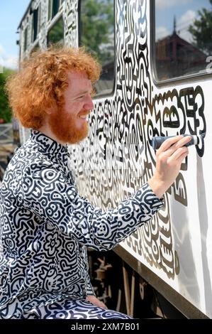 Tenterden, Kent, Royaume-Uni. 26 juillet 2024. L'artiste de renommée internationale Mr Doodle (Sam Cox) crée le premier train Doodle au monde, couvrant un wagon de 64 pieds avec ses griffes signature - pour marquer le 50e anniversaire du chemin de fer Kent et East Sussex, à sa base à la gare de Tenterden dans sa ville natale. Crédit : Phil Robinson/Alamy Live News Banque D'Images