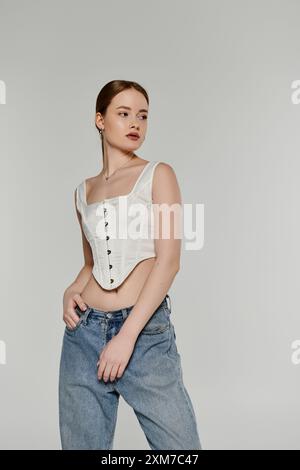 Une jeune femme pose en toute confiance, portant un corset blanc et un Jean denim. Banque D'Images