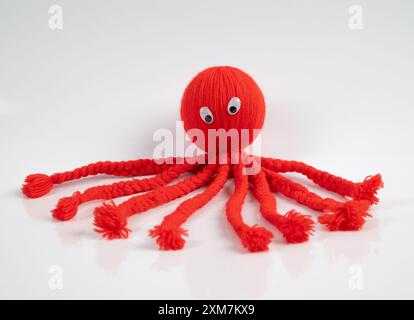 Jouet de marionnette de poulpe rouge sur un fond blanc, fait à la main en laine douce. Cette adorable poupée rigide est tricotée avec amour pour le plaisir. Banque D'Images