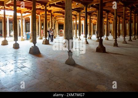 Les visiteurs se promènent parmi des colonnes de bois finement sculptées à l'intérieur de la mosquée historique Juma à Khiva, en Ouzbékistan Banque D'Images