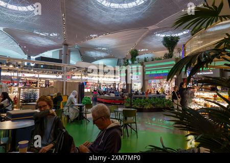 Vue intérieure animée du terminal de l'aéroport d'Istanbul avec les voyageurs assis dans une aire de restauration entourée de boutiques sous un plafond moderne Banque D'Images