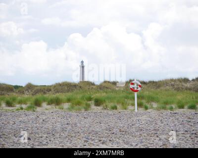 Bouée de sauvetage rouge et blanche sur la plage de Skagen, Danemark, à l'arrière-plan d'un phare. Bouée de sauvetage. Concept de préservation de sauveteur. Banque D'Images