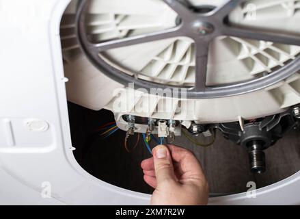 La main du maître retire les puces électriques pour retirer l'élément chauffant de la machine à laver et le capteur de chauffage. Réparation du lavage mac Banque D'Images