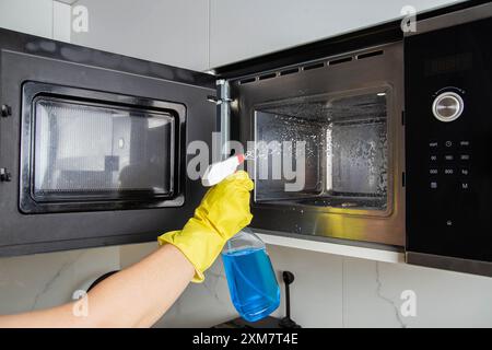 Spray anti-graisse dans la main d'une fille qui nettoie la cuisine. Nettoyer le four à micro-ondes de la graisse et de la saleté. Agent antistatique moderne. Banque D'Images