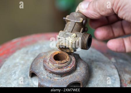 Une valve cassée d'une bouteille de gaz dans une main contre le fond d'une bouteille de gaz rouge. Fuite de gaz propane et concept d'explosion. Banque D'Images