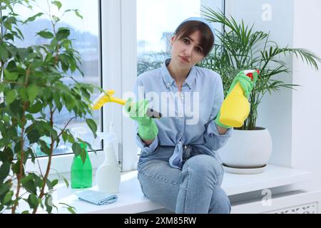 Jeune femme fatiguée avec raclette, vaporisateurs de détergent et serviette sur le rebord de la fenêtre à l'intérieur Banque D'Images