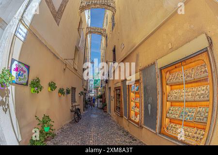 ALGHERO, SARDAIGNE, ITALIE-4 JUILLET 2024 : vue le long de la rue médiévale et commerciale Carrero de L'arsenal-Vicolo Serra, avec de petites boutiques traditionnelles Banque D'Images