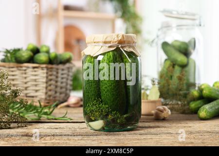 Concombres marinés dans un pot et ingrédients sur une table en bois, gros plan Banque D'Images