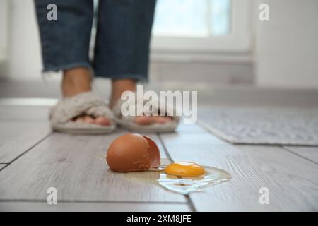 Femme près de l'oeuf cru cassé sur plancher en bois gris à l'intérieur, foyer sélectif Banque D'Images