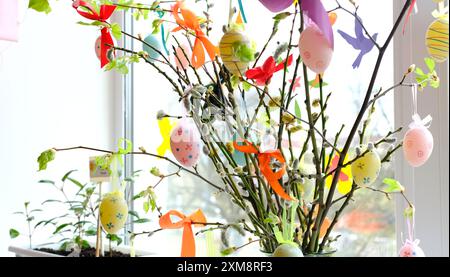 Décorations lumineuses d'oeufs de Pâques suspendues sur des branches de saule dans un vase, créant une atmosphère festive et joyeuse. Banque D'Images