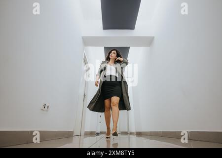 Femme d'affaires confiante avance dans le couloir moderne avec téléphone. Banque D'Images