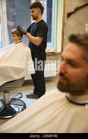 Barbier barbu masculin faisant une coupe de cheveux élégante à petit garçon Banque D'Images