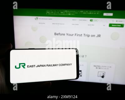 Personne tenant un smartphone avec le logo de l'entreprise ferroviaire japonaise East Japan Railway Company en face du site Web. Concentrez-vous sur l'affichage du téléphone. Banque D'Images