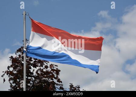 Le drapeau national des pays-Bas flotte sur un mât de drapeau par une belle journée d'été avec un fond de ciel bleu et de nuages blancs. Banque D'Images