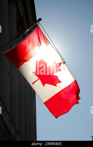 Le drapeau canadien est suspendu à un bâtiment du centre-ville d'Ottawa, Ontario, Canada, avec un fond de ciel bleu brillant. Banque D'Images