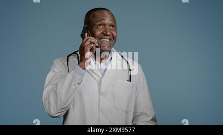 Adulte africain américain homme médecin parlant au téléphone avec le patient dans le fond bleu studio thérapeute mâle dans la robe médicale consulter le client en utilisant Banque D'Images