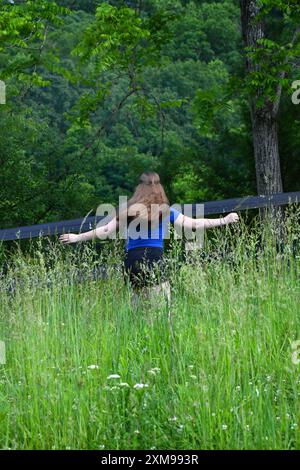 Adolescent tournoie de manière ludique dans l'herbe verte haute. Ses cheveux se balancent derrière elle. Elle porte une chemise bleue et un short noir. Banque D'Images