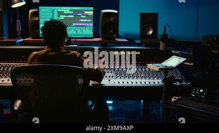 Concepteur sonore afro-américain éditant des enregistrements audio dans la salle de contrôle, travaillant avec des mélangeurs et des faders sur la console de mixage. Producteur de musique créant de nouveaux morceaux et pistes. Caméra B. Banque D'Images