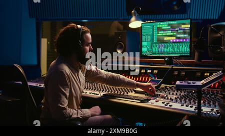 Ingénieur mixeur appuyant sur les curseurs sur le pupitre de commande pour équilibrer les pistes et ajouter des effets sonores, créant de la nouvelle musique. Expert en ingénierie audio travaille avec des faders motorisés en studio professionnel. Caméra B. Banque D'Images