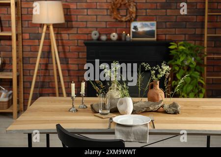 Ensemble de vaisselle propre, vases avec de belles fleurs, des pierres et des bougies allumées sur une table en bois dans une salle à manger élégante Banque D'Images