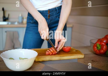 Vue rapprochée des mains féminines coupant des tomates fraîches sur une planche à découper en bois dans une cuisine en bois Banque D'Images