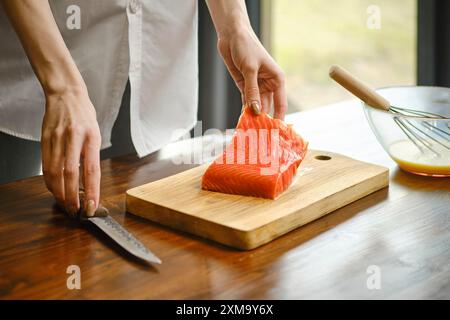 Femme méconnaissable va couper le filet de truite fumée en tranches sur une planche à découper en bois Banque D'Images