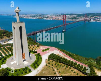 Une grande statue aux bras tendus se dresse sur un point de vue près d'un pont sur l'eau, avec une ville en arrière-plan, vue aérienne, Statue Cristo Rei Banque D'Images