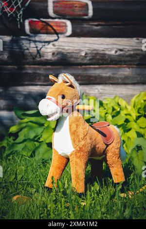 Un cheval jouet en peluche sur une pelouse herbeuse dans un jardin avec un mur en bois et un panier de basket-ball en arrière-plan Banque D'Images