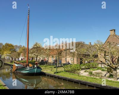 Un bateau à voile traditionnel amarré sur un canal devant des maisons historiques avec des arbres et des jardins au printemps, enkhuizen, pays-bas Banque D'Images