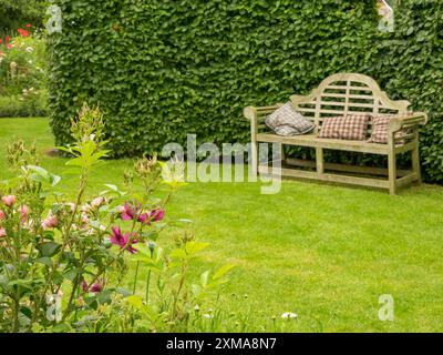 Un banc de jardin avec des coussins devant une pelouse taillée et des fleurs roses et une haie verte, borken, westphalie, allemagne Banque D'Images