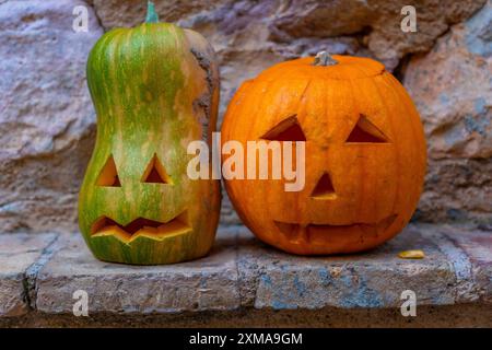 Deux citrouilles avec des visages sculptés en eux sont assis sur un rebord. Les citrouilles sont orange et vertes, et elles semblent être dans un décor sur le thème d'Halloween Banque D'Images