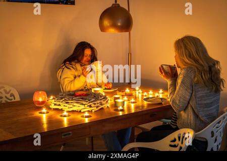 Image symbolique économie d'énergie, hiver froid, crise énergétique, plat froid, mère et fille vêtues chaudement au dîner, seulement à la lueur des chandelles, chauffage sur Banque D'Images