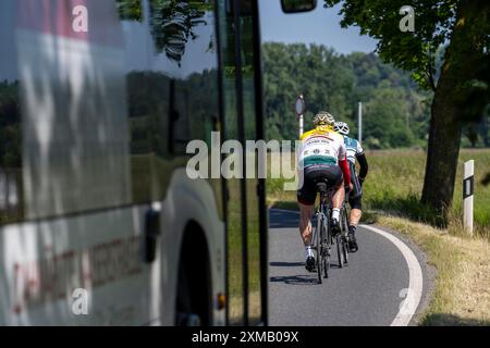 Cycliste de route sur une route de campagne suivie d'un bus local qui ne peut pas dépasser les cyclistes dans un virage Banque D'Images