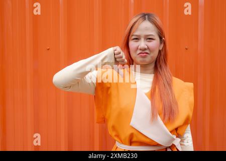 Portrait de belle femme asiatique donnant le pouce vers le bas sur fond orange Banque D'Images