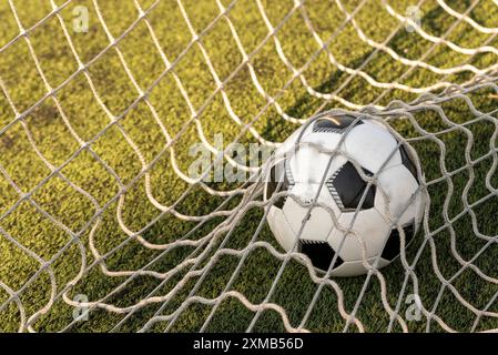 Un ballon de football noir et blanc propulsé par un puissant tir, déchirant à travers le filet dans un but parfait. Le maillage renflé souligne l'impact et le prec Banque D'Images