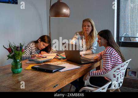 Homeschooling, pendant le confinement en janvier 2021, mère aide ses deux filles, à la maison, à apprendre, avec des manuels et des ordinateurs, des fermetures d'écoles Banque D'Images