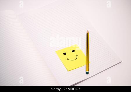 Une note collante jaune avec un smiley dessus est assis sur le dessus d'un crayon. Le crayon est jaune et a une gomme noire. Concept de bonheur et pos Banque D'Images