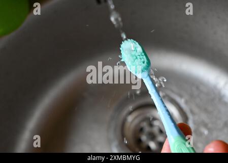 une brosse à dents bleue est aspergée d'eau provenant d'un robinet Banque D'Images