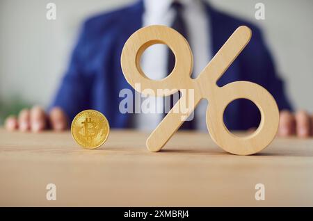 Commerçant d'actions homme portant costume assis au bureau dans le bureau avec bitcoin et signe de pourcentage sur la table. Banque D'Images