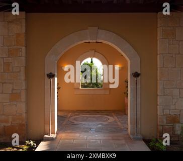 Une antichambre avec une arche ronde et un sol en mosaïque. Une fenêtre de jardin donne sur un jardin luxuriant fleuri. Le Luxury Aphrodite Hills Hotel and Resort Buil Banque D'Images