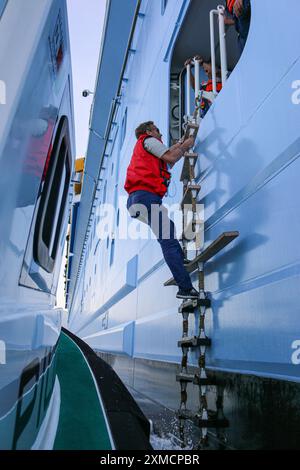 Nice, France : bateau pilote portuaire approchant l'HYMNE DES MERS géant de Royal Caribbean pour embarquer le pilote maritime à Villefranche sur mer. Une escale unique pour le plus grand bateau de croisière cette année dans le petit port de la Côte d'Azur. Après la saison estivale, l'impressionnant navire devait naviguer à travers le canal de Suez dans le cadre d'un repositionnement de l'Europe vers un nouveau port d'attache à Singapour, mais à la suite des tensions de la mer Rouge et des menaces d'attaques de missiles Houthi sur les navires, il transportera plutôt sans passager autour de la pointe sud de l'Afrique pour rejoindre Dubaï et l'Asie. Crédit : Kevin Izorce/Alamy Live News Banque D'Images